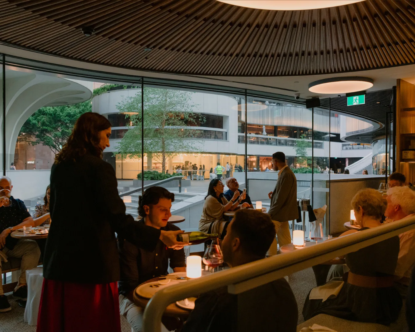 The upstairs interior of Aalia Wine Room. A sommelier pours a glass of wine with a view out to Martin Place.