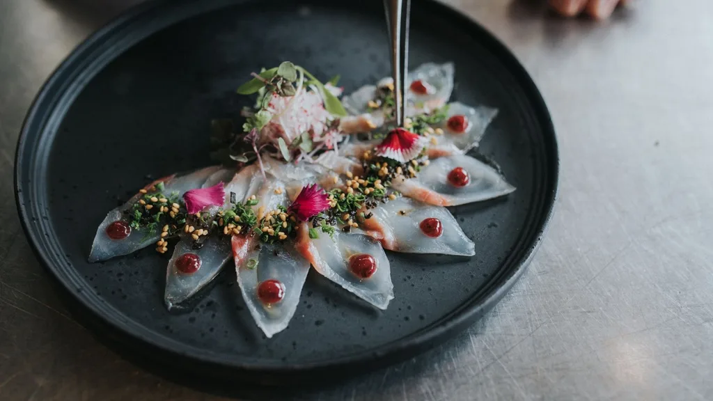 A black plate of raw kingfish sashimi with pink and green garnishes from Yamagen restaurant on the Gold Coast