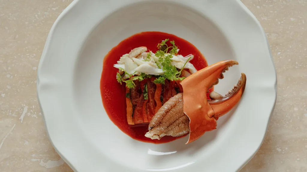 a large crab claw on a white plate elegantly presented with crab meat and a red jus at Esmay in Adelaide