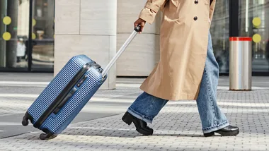 woman with suitcase walking outdoors in city by airport or train station