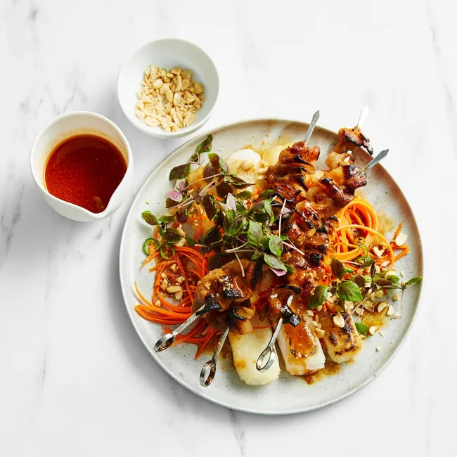 Pork skewers sticky with a chilli-caramel glaze is served on a bed of crisp rice noodles