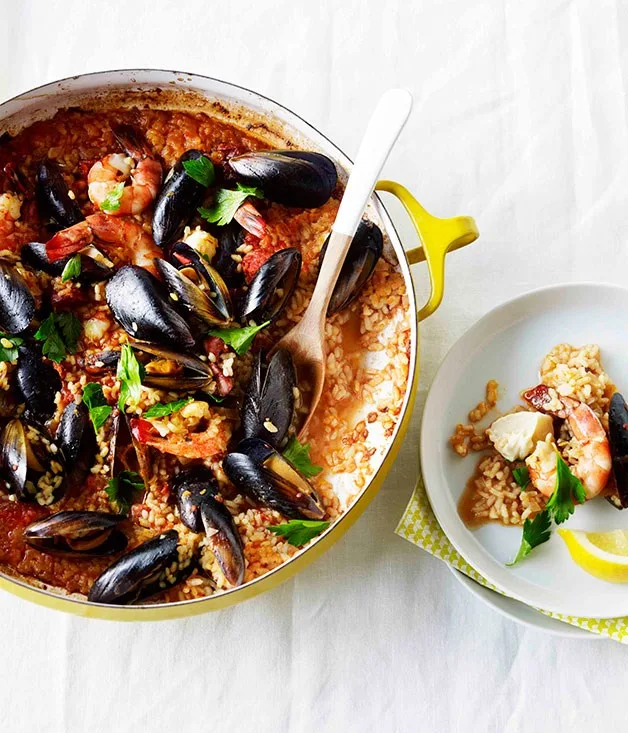 one pan dinner of Spanish-style seafood saffron rice dish in a yellow pot against white background