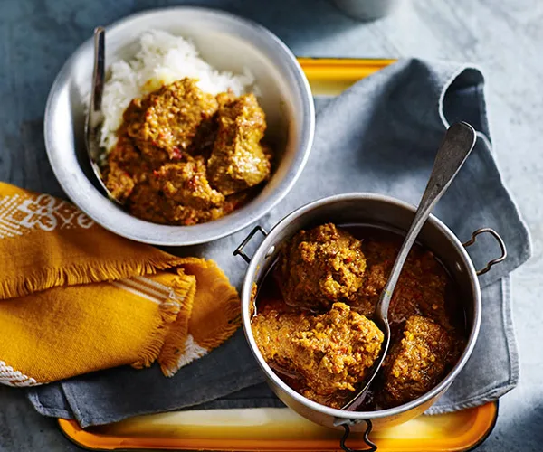 Two bowls with slow-cooked beef rendang curry, on a golden square tray with mustard-yellow and blue napkins.