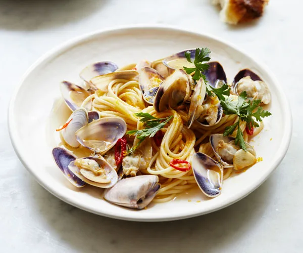 A white plate holding spaghetti, clams, chilli and flat-leaf parsley.