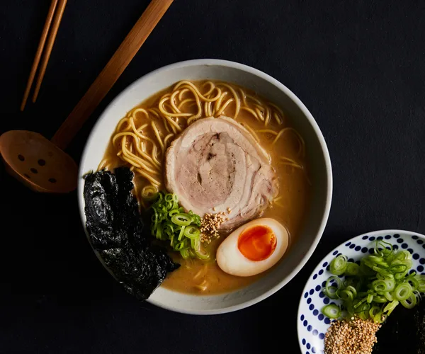 Japanese ramen recipe topped with half a boiled egg, a slice of pork, nori and chopped spring onion