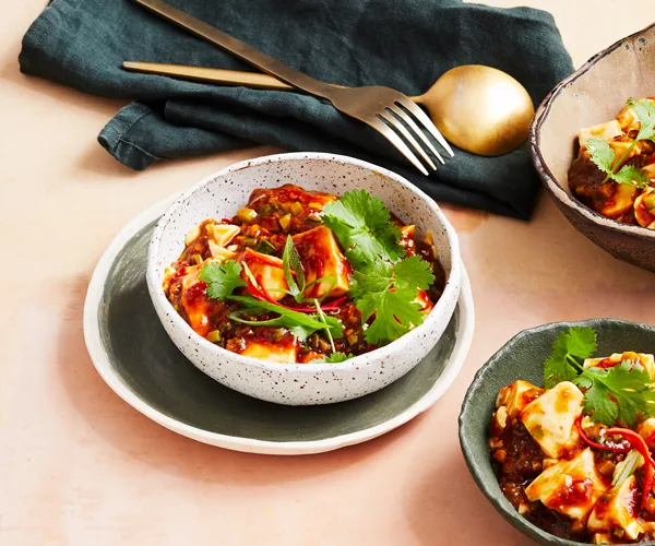 Ma po tofu in a white bowl with a green napkin and brass cutlery in the background