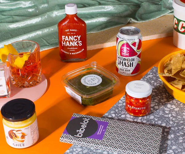 An assortment of grocery items – a bottle of chilli sauce, ghee, chocolate, dip – on an orange table