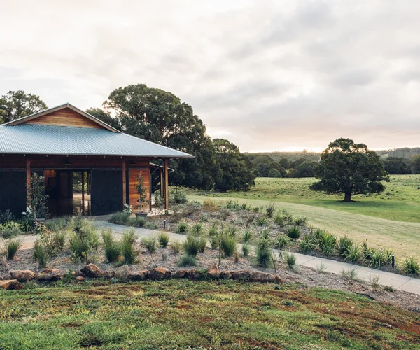 Modern converted barn with a pitched roof, with a path leading up to its doors, on a grassy paddock