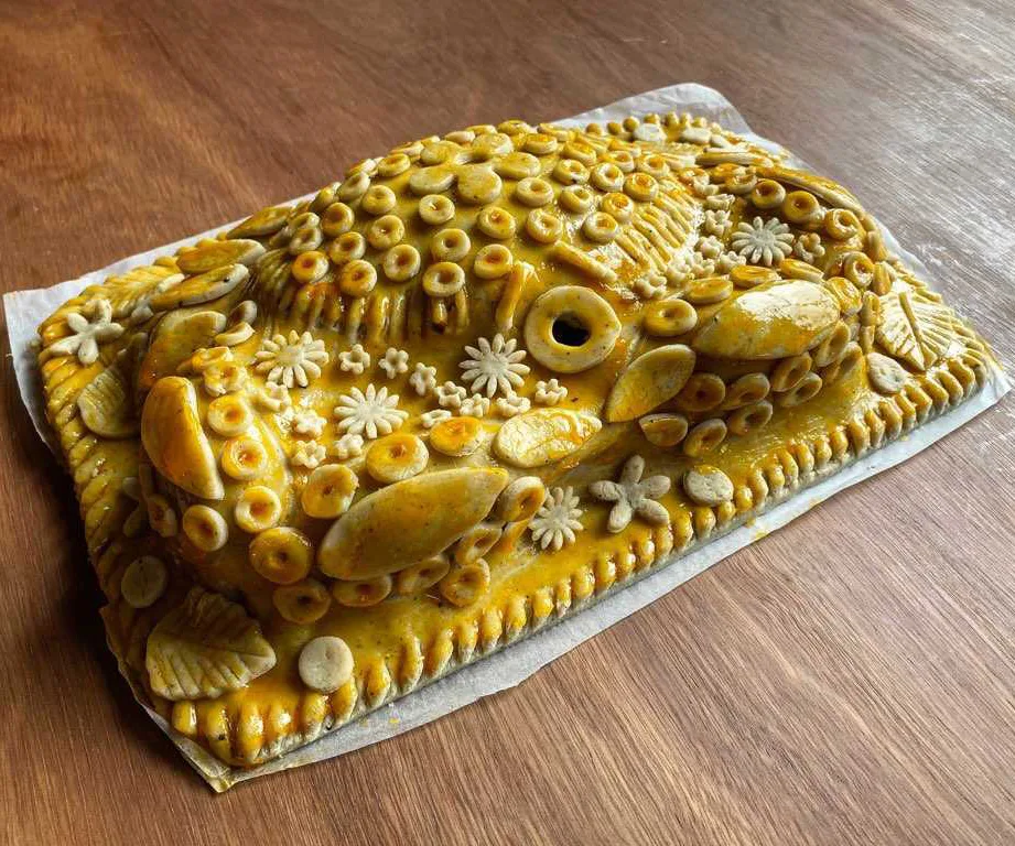 A whole mud crab, draped in baked pastry, and decorated with pastry flowers, circles and patterns. It sits on a brown wooden table.