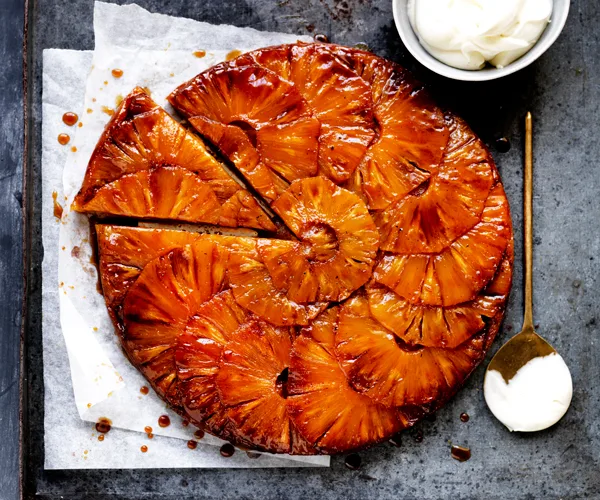 Upside-down tart with caramelised pineapple slices layered on top, with a triangular slice detached from the tart. 