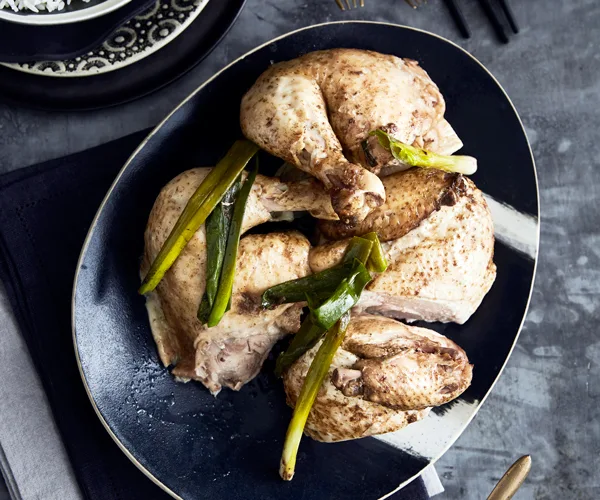 A black egg-shaped platter holding large chopped pieces of roast chicken and spring onions.