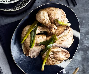 A black egg-shaped platter holding large chopped pieces of roast chicken and spring onions.