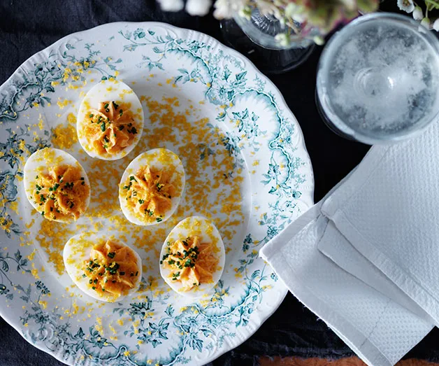 Deviled eggs garnished with herbs on a decorative plate beside a glass of water and folded napkins.