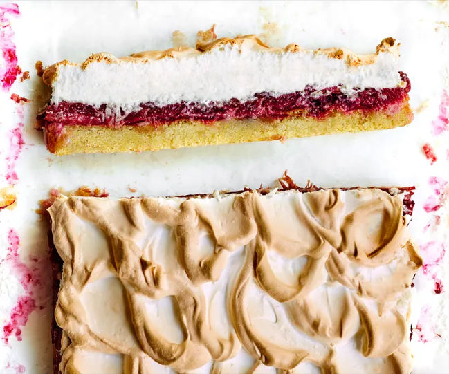 Raspberry and meringue tart on a white surface, partially sliced, showing layers of meringue, raspberry, and pastry.