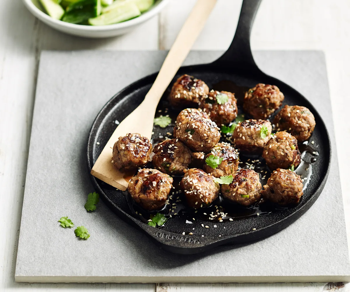 A flat black cast-iron pan with small fried meatballs, sprinkled with white sesame seeds.