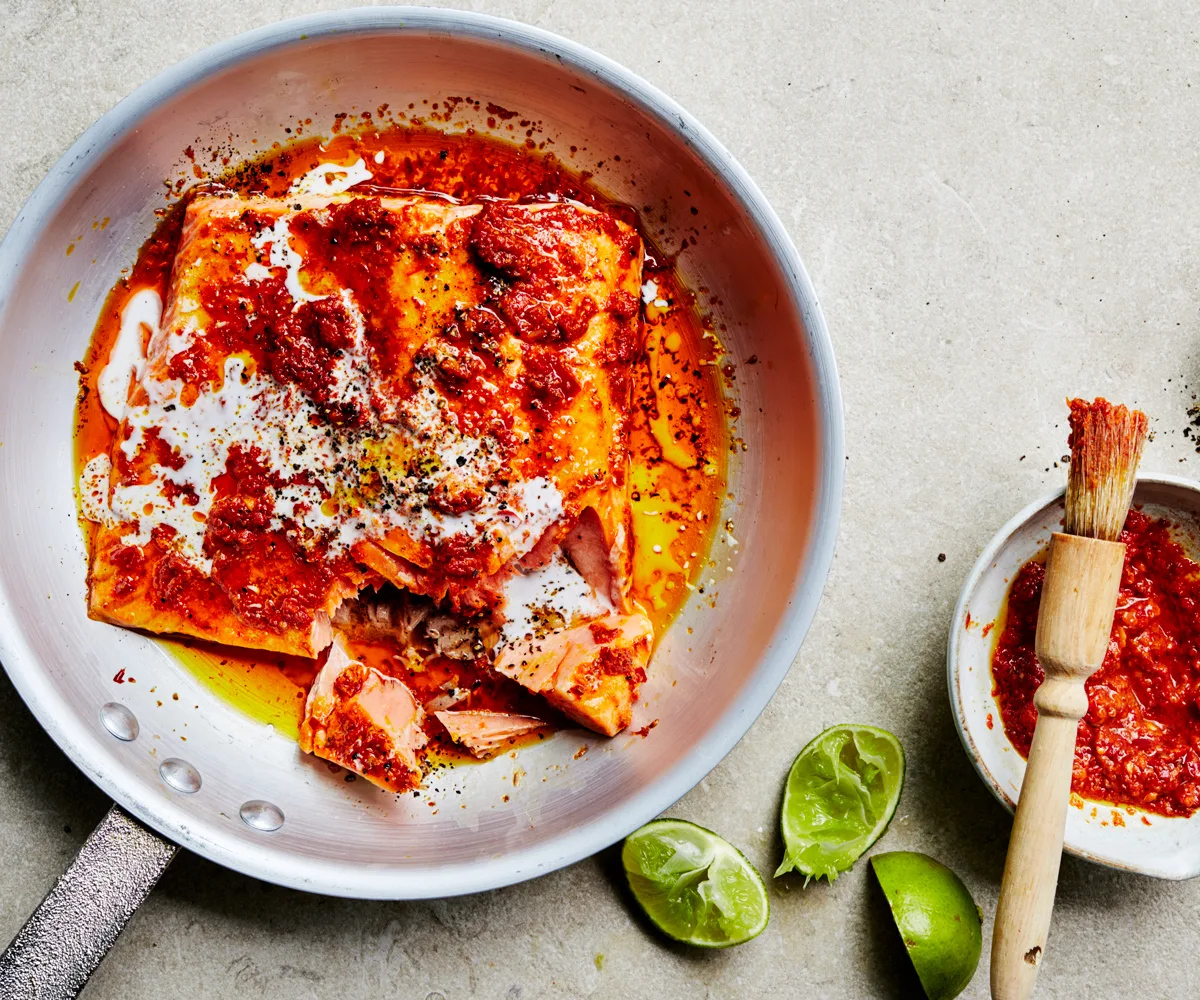 Over-the-top image of round metal frying pan, with pink ocean trout coated in a red chilli paste and drizzled with yoghurt.