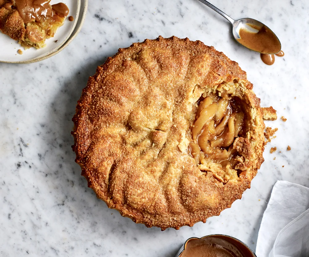 Overhead shot of a crusty apple pie with a bit spoonful taken out of the right hand side.