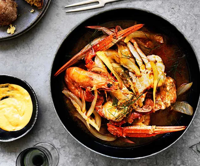 Seafood dish with crab and shrimp served in a black bowl, accompanied by dipping sauce on a gray surface.