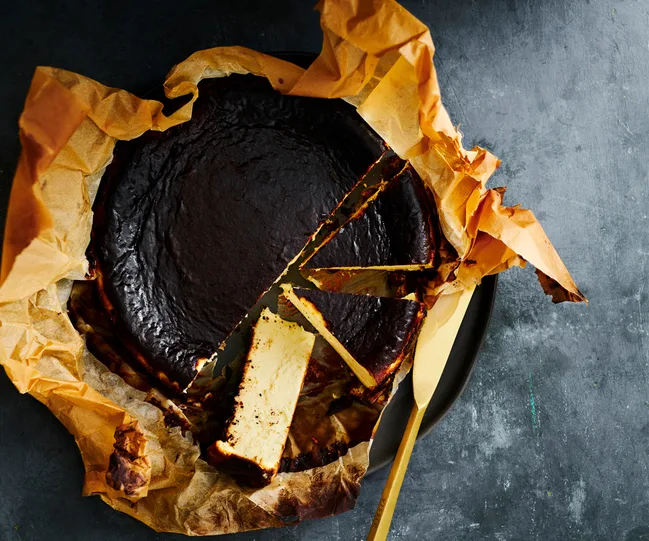 Burnt Basque cheesecake on parchment paper, partially sliced, with a golden serving knife beside it.