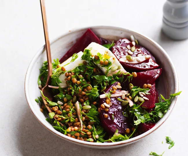 Bowl of beetroot salad with feta, herbs, lentils, and seeds, featuring a fork on the side.
