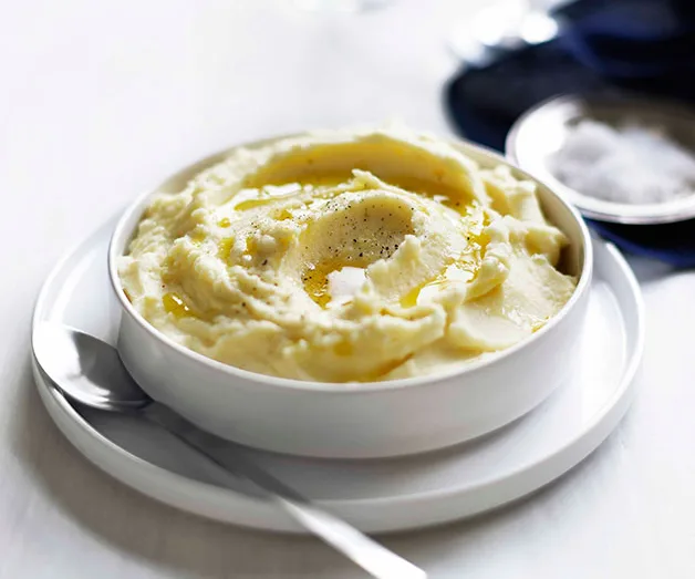 A white dish holding creamy mashed potato, with a grind of black pepper on top.