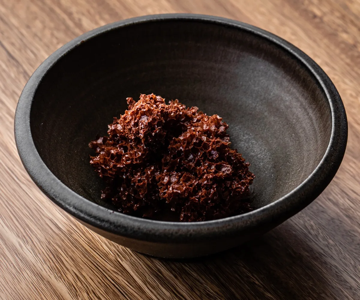 A chocolate, coral-like mousse in a dark black bowl on a bench.