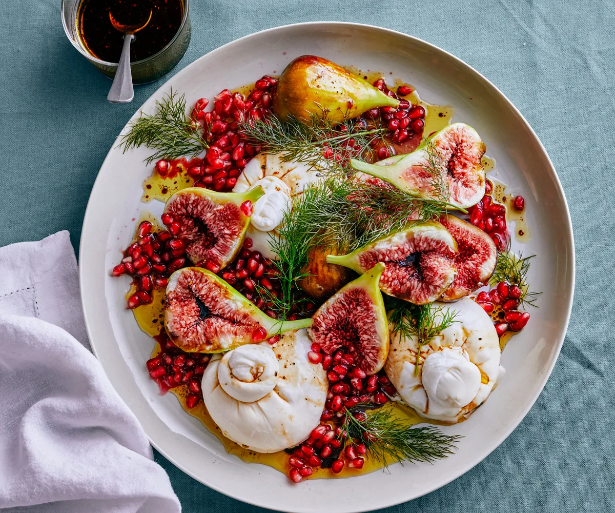 A large plate of figs with burrata, garnished with pomegranate arils and fennel sprigs