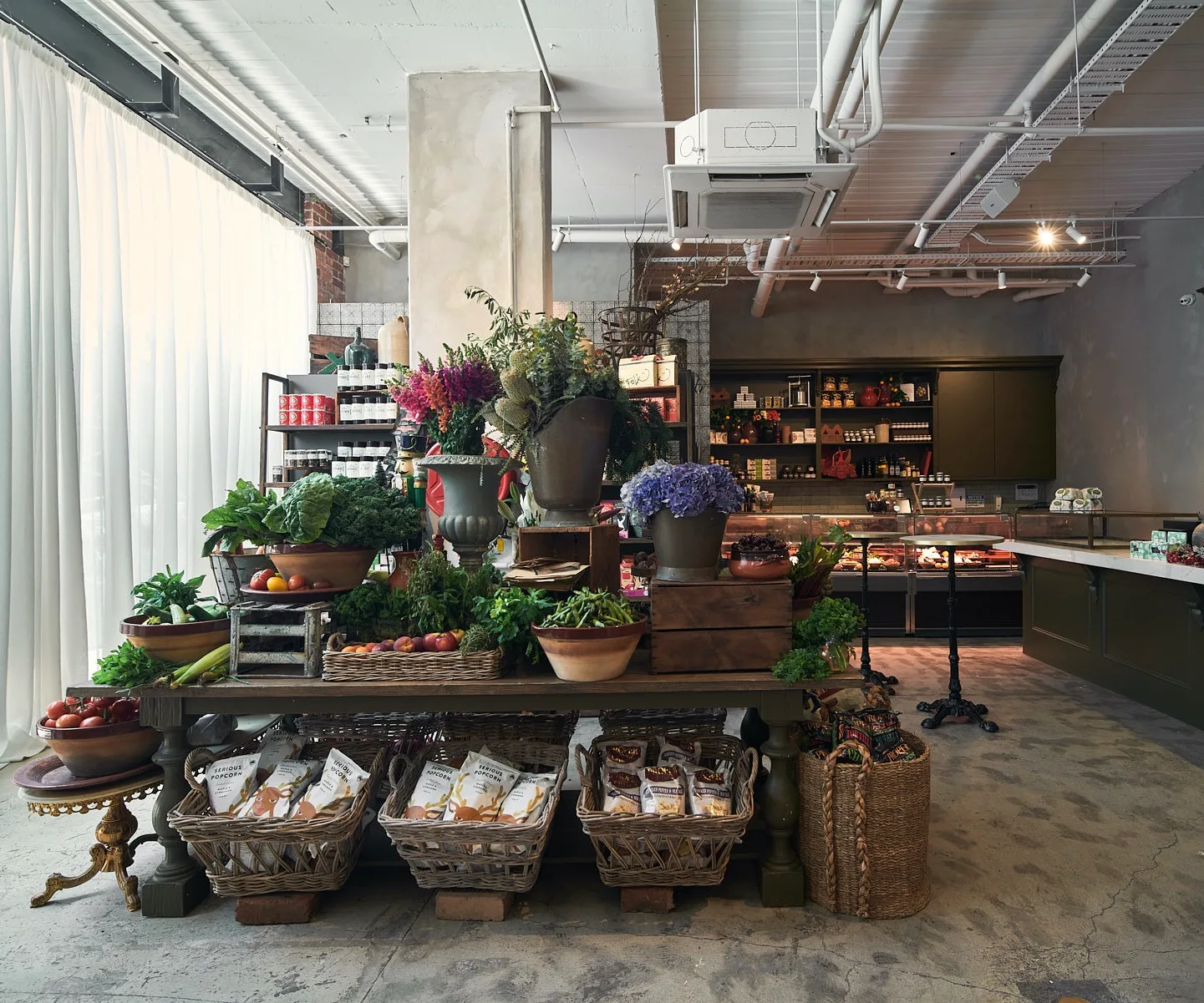 There's a table full of flowers and vegetables, below it is a range of vegan products. In the background, there is a shop counter with shelves behind it.