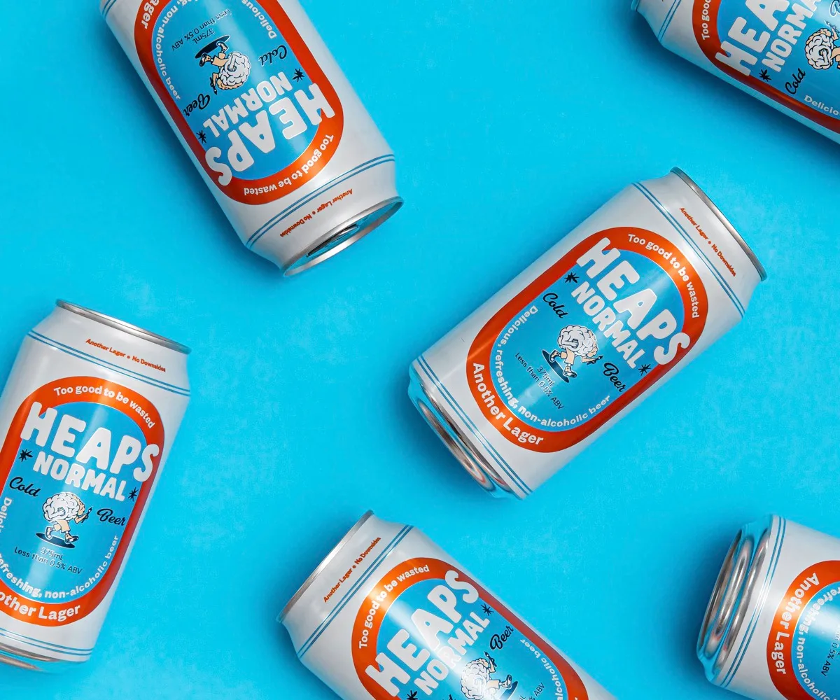 Cans of Heaps Normal's new beer, Another Lager, set against a light blue background.