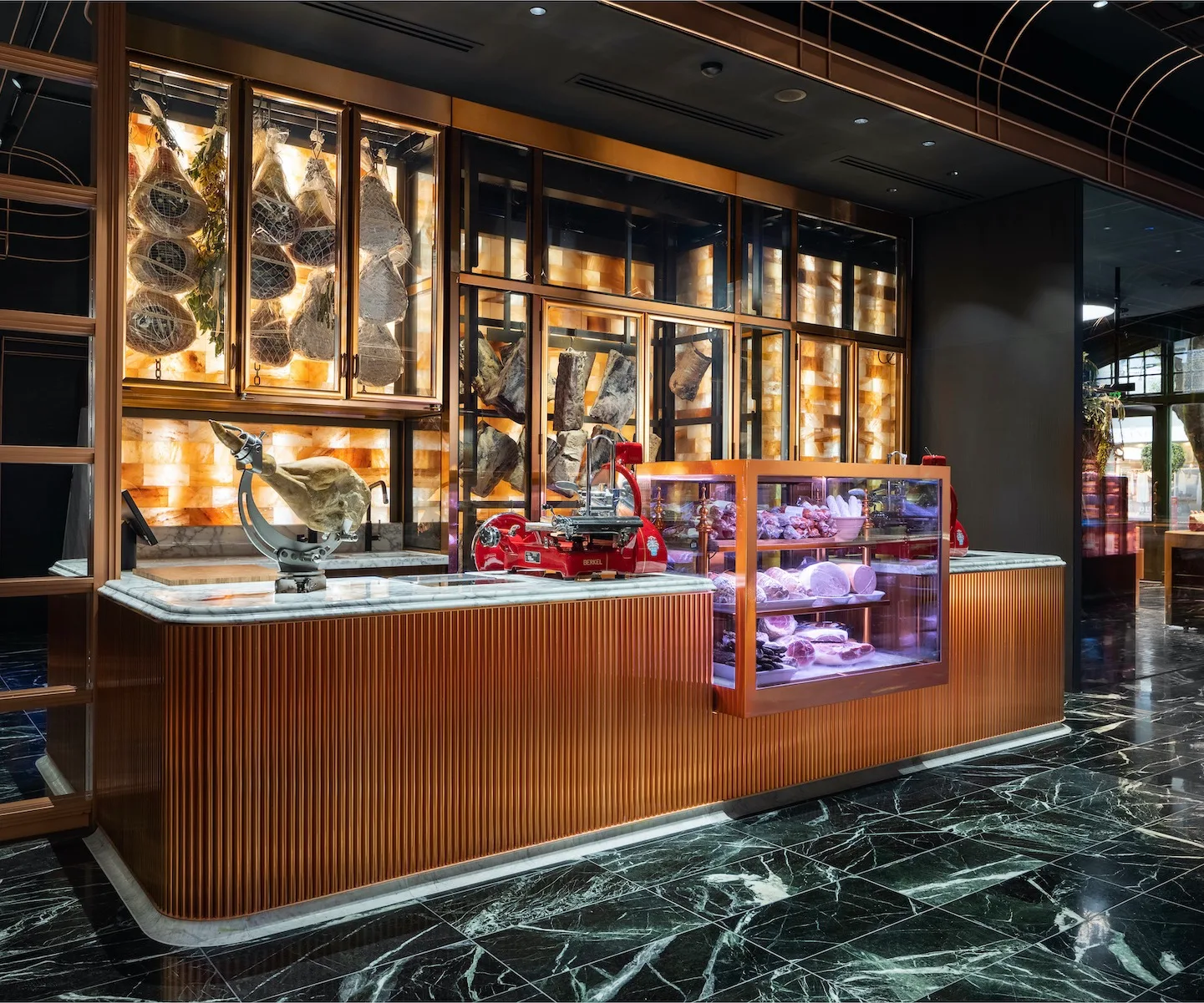 A wooden counter with marble countertops. Behind there are glass cabinets filled with dried and cured meats.