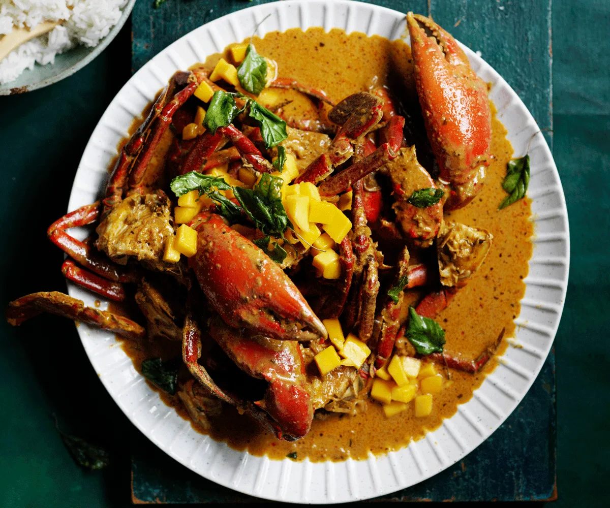 Red chilli crab with mango and basil leaves on a white plate (aerial view).