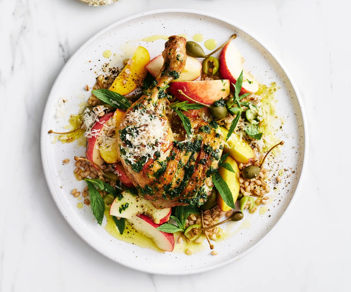 Charred chicken Maryland served on pearl barley salad with nectarine slices and topped with parmesan on a white plate.