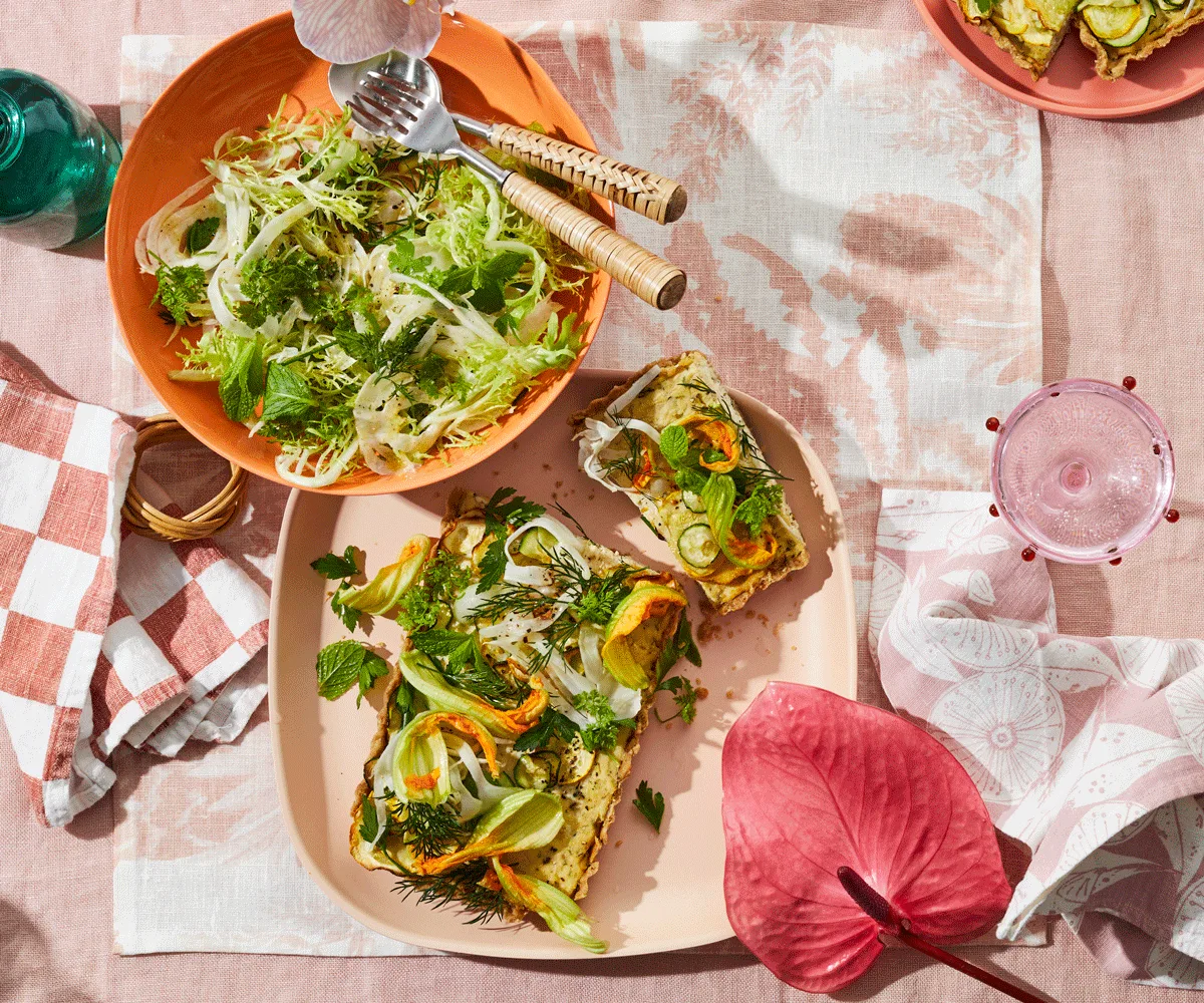 orange-bowl-filled-with fennel-salad-next-to-a-plate-with-whipped-tofu tart topped with zucchini flowers and more fennel salad.