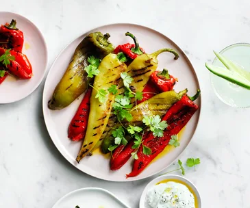 Char-grilled red and green peppers on a white plate topped with flat-leaf parsley and drizzled with olive oil served on a white plate.