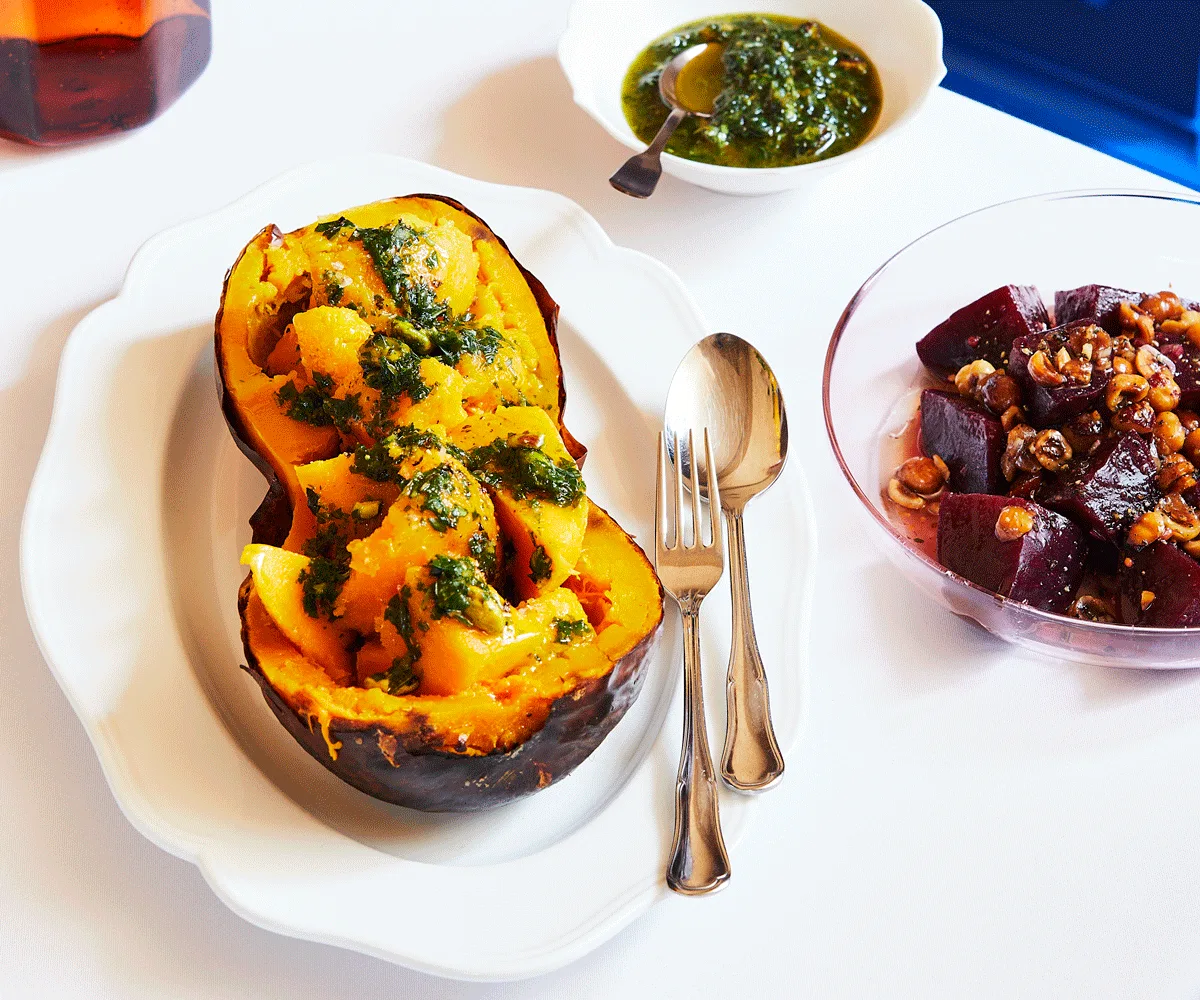 A butternut pumpkin split in half lengthwise, roasted, with large chunks of the flesh served inside the roasted half, topped with pistachio pesto