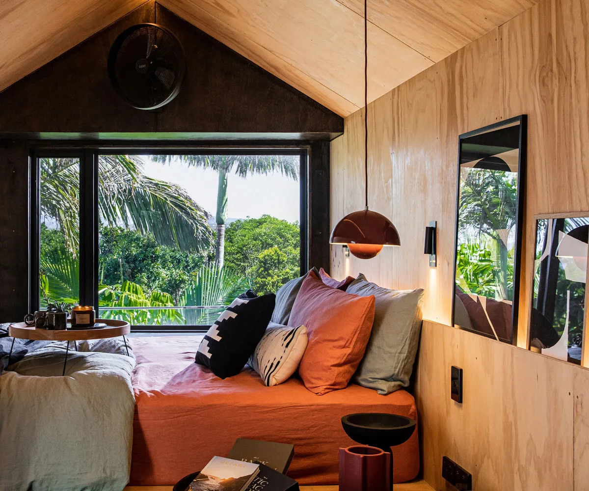 Interior of a tiny home cabin with pendant light, bed with orange and green sheets and large window