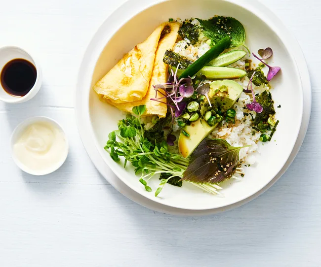Bird's eye view of white bowl filled with white rice, green vegetables, herbs and egg