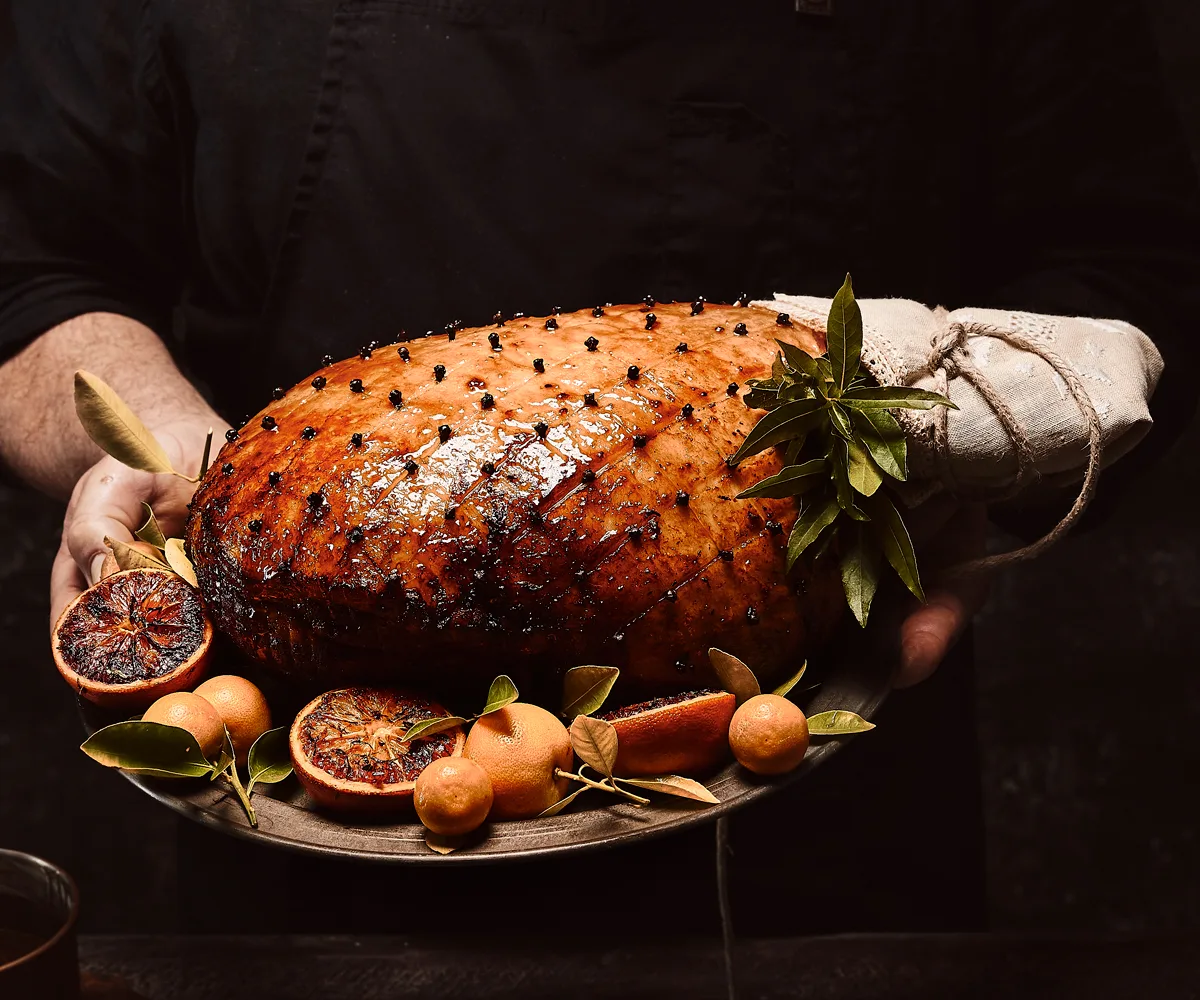 Best christmas hams australia to buy - glazed christmas ham on platter, surrounded by halved blood oranges and whole orange cirtus