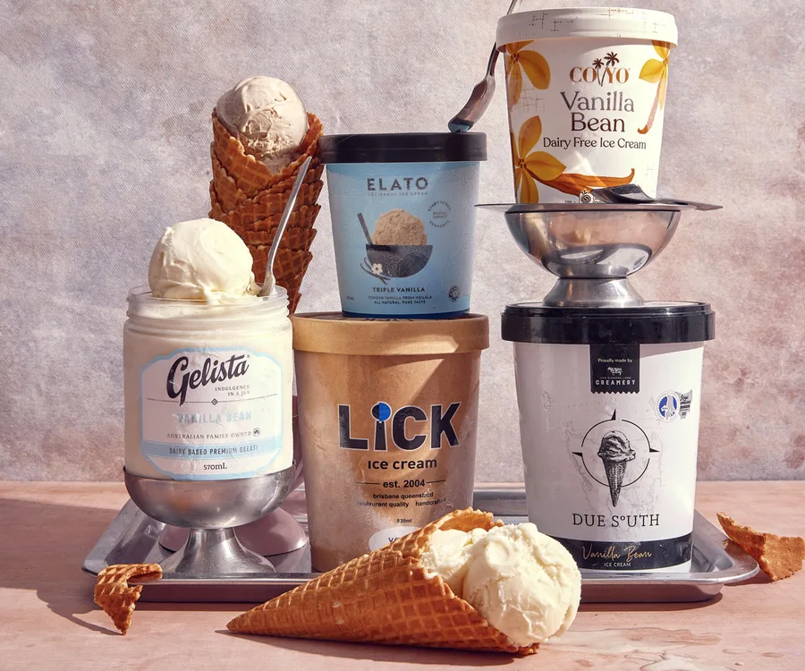 Five tubs of vanilla ice cream lined up with scoops in waffle cones to decorate