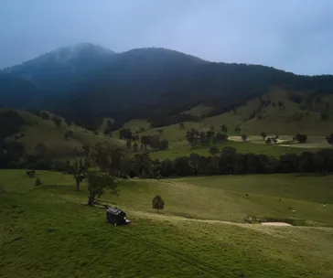 green paddock with two small dams, a black tiny cabin and a mountain with fog covering in the background