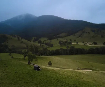 green paddock with two small dams, a black tiny cabin and a mountain with fog covering in the background