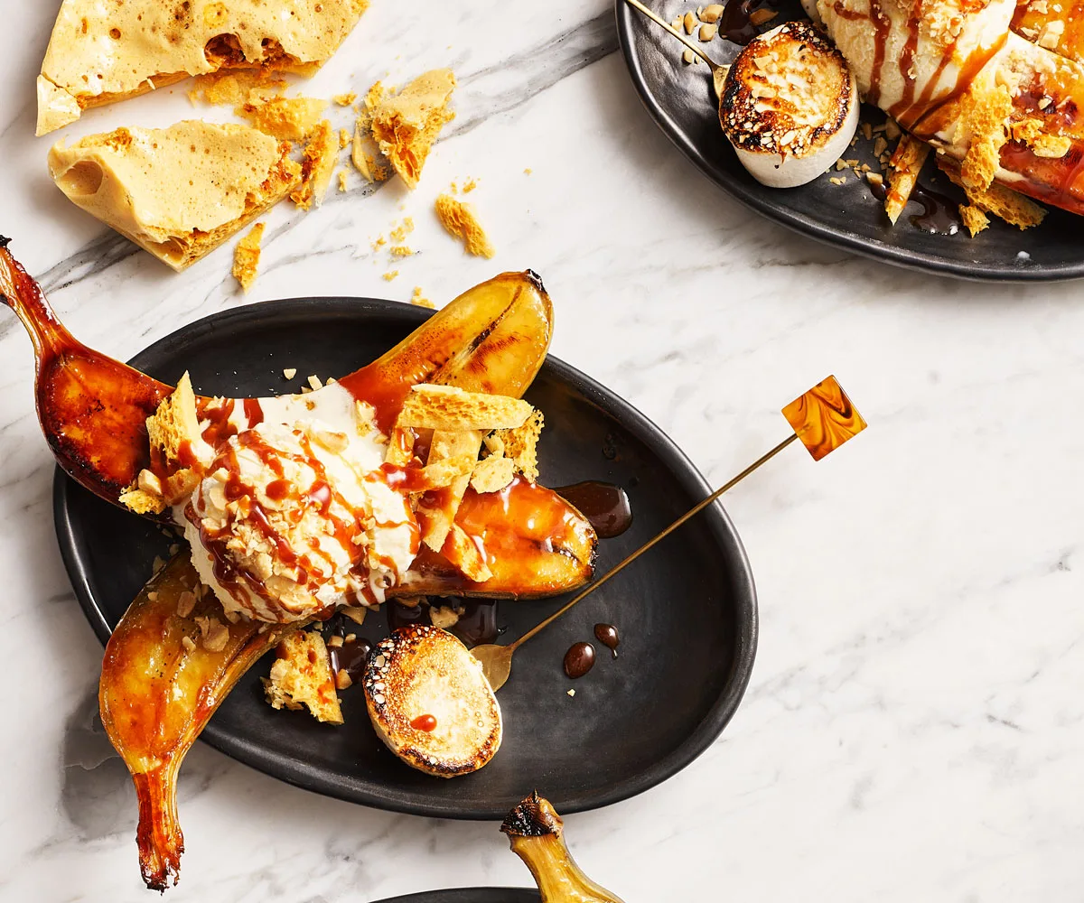 Photo of halved bananas on black plate, topped with ice cream and caramel