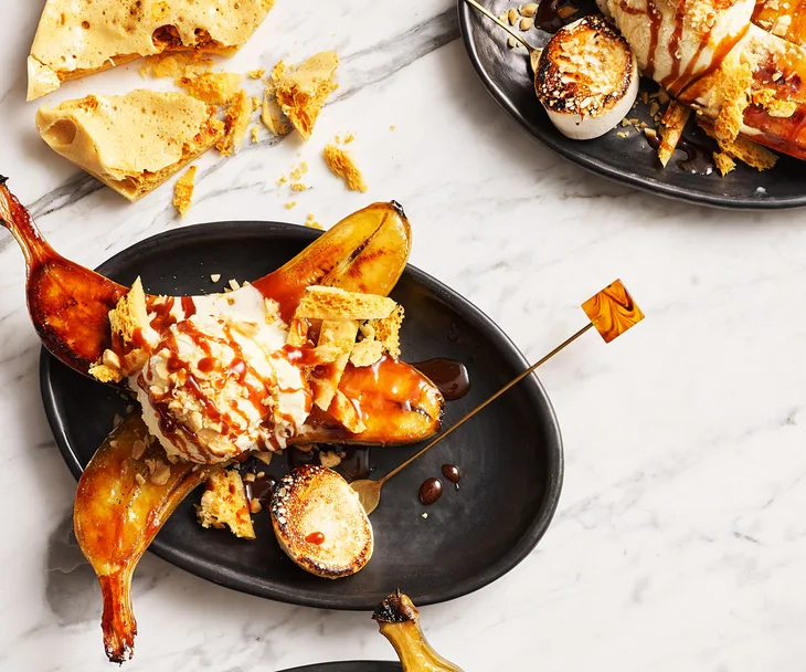 Photo of halved bananas on black plate, topped with ice cream and caramel