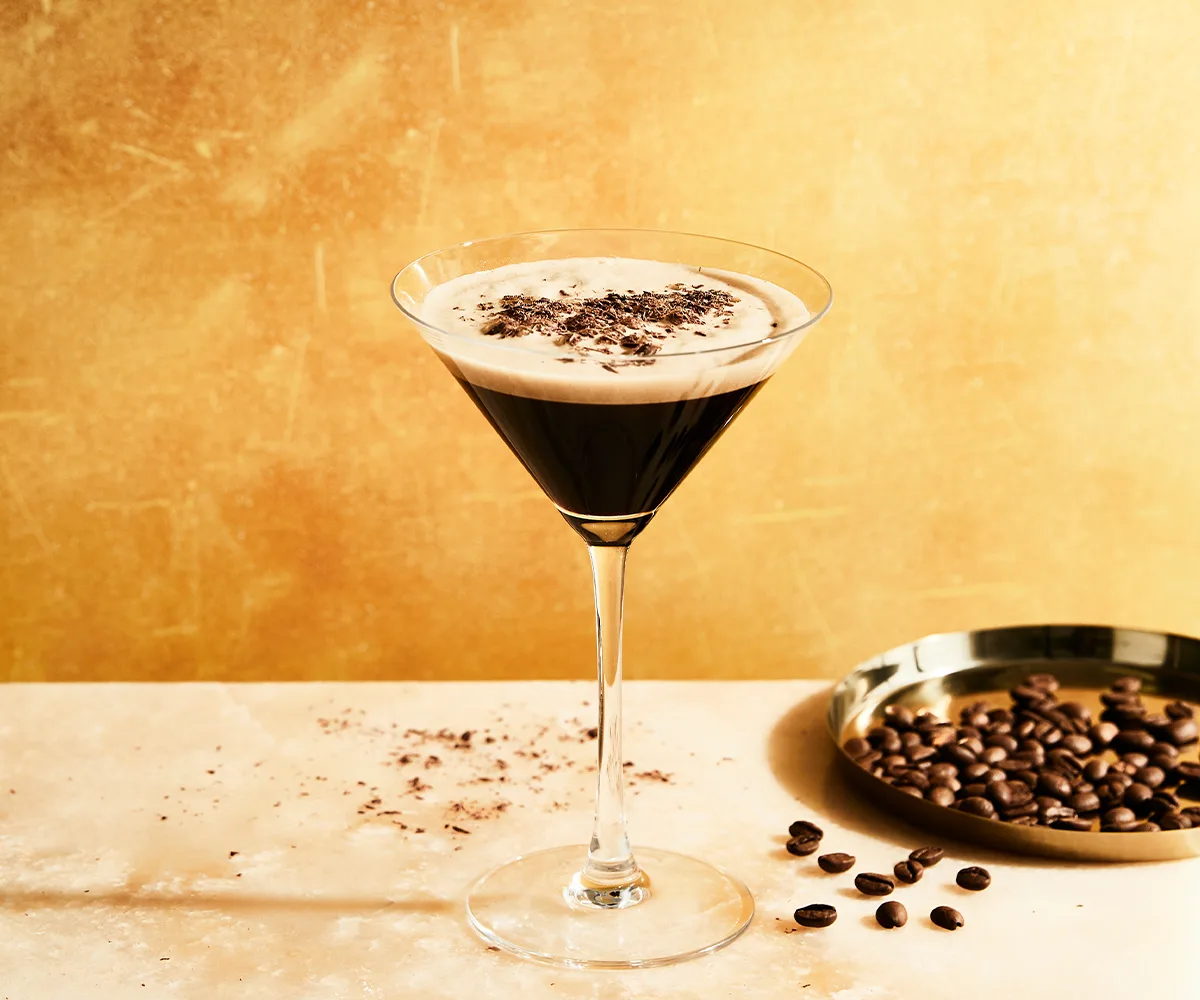 Single Espresso Martini in a martini glass next to a silver dish of coffee beans