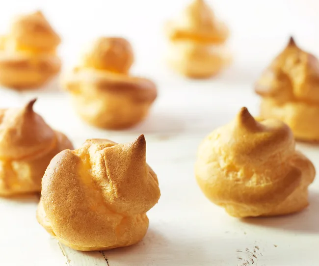 Cream puffs on a white wooden surface, golden brown and crisp.