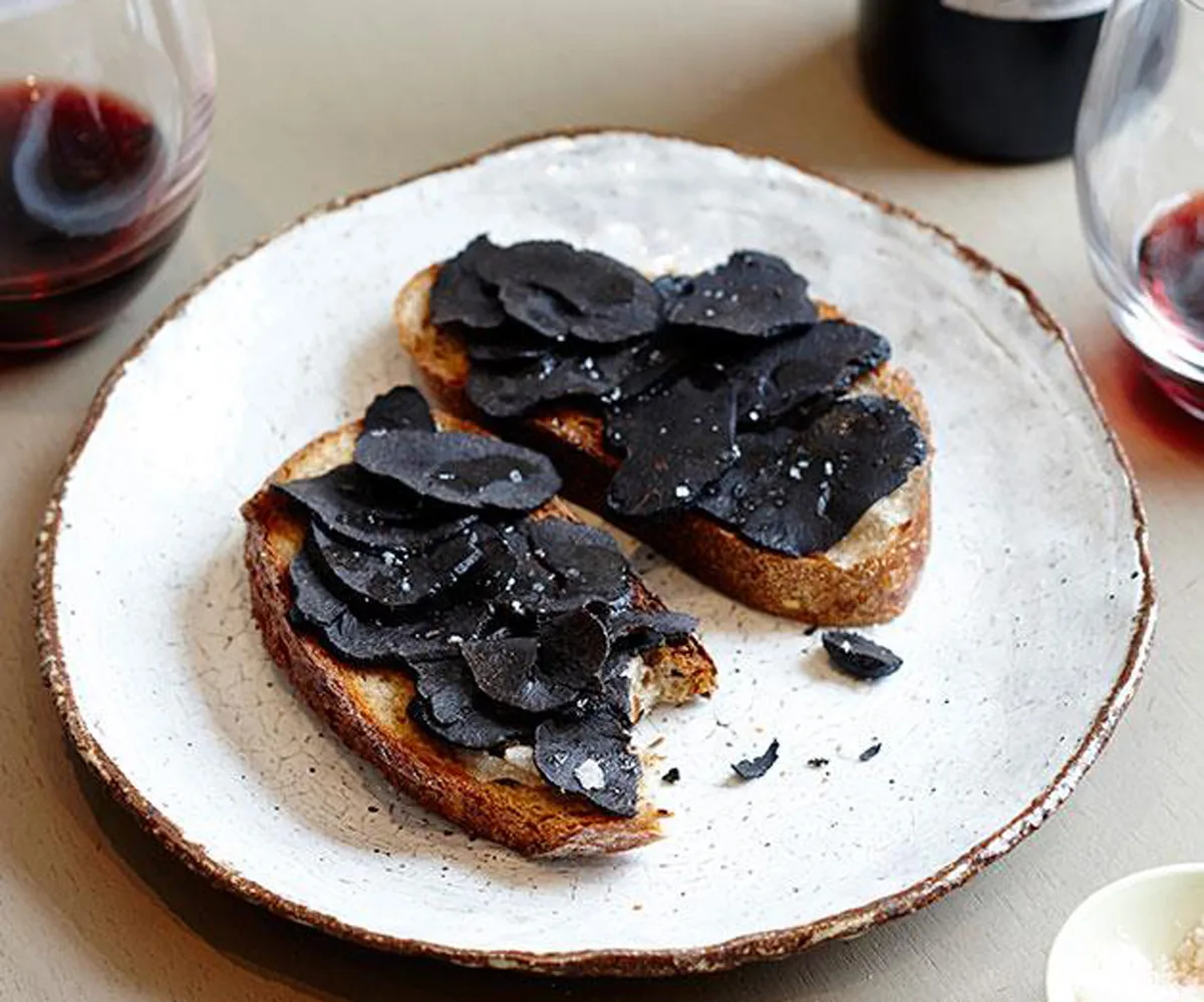 Two sliced of bread topped with round flakes of black truffles and salt