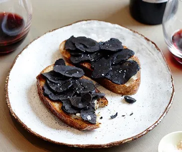 Two sliced of bread topped with round flakes of black truffles and salt