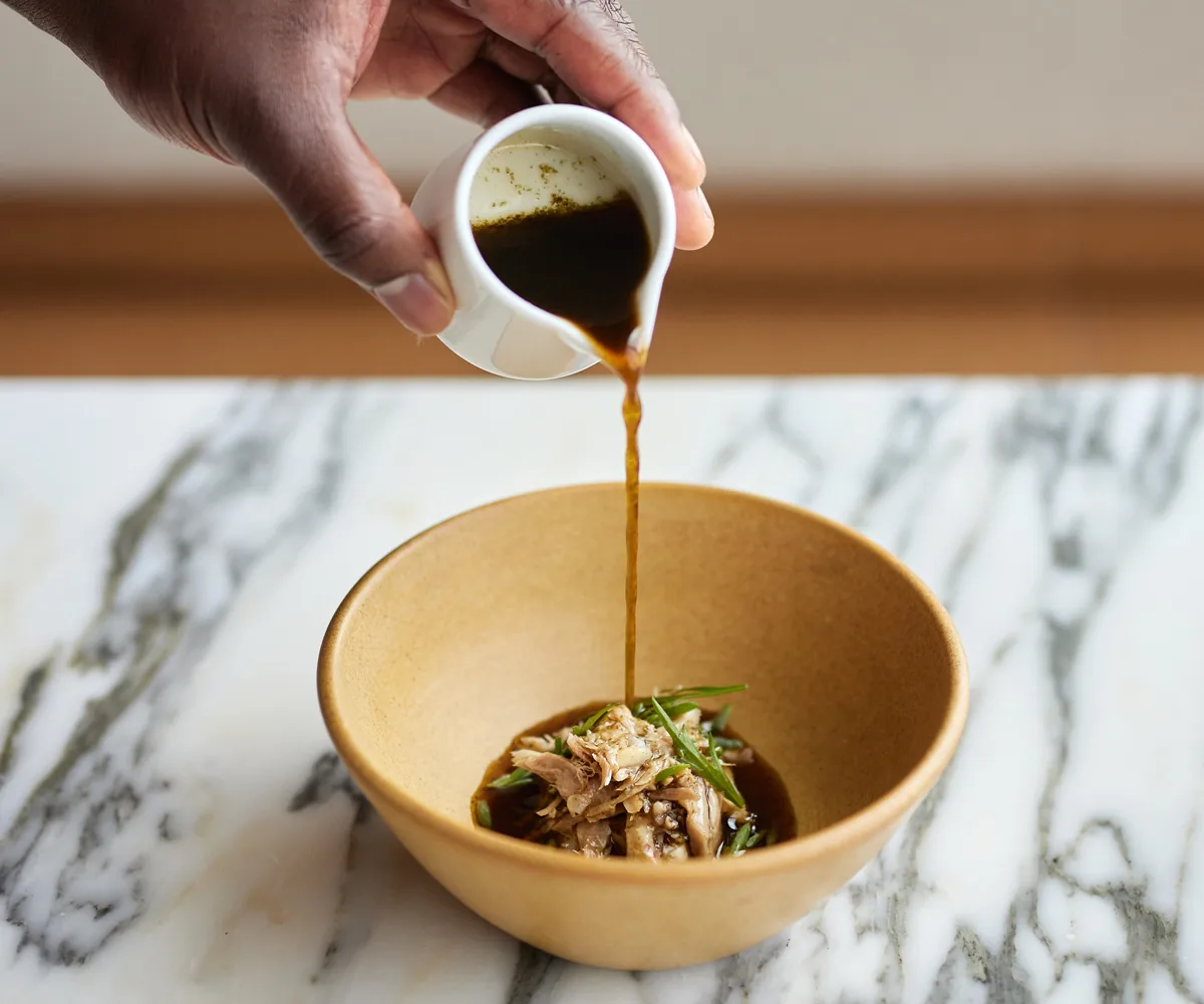 Brown liquid being pourned into a yellow bowl filled with native Australian ingredients