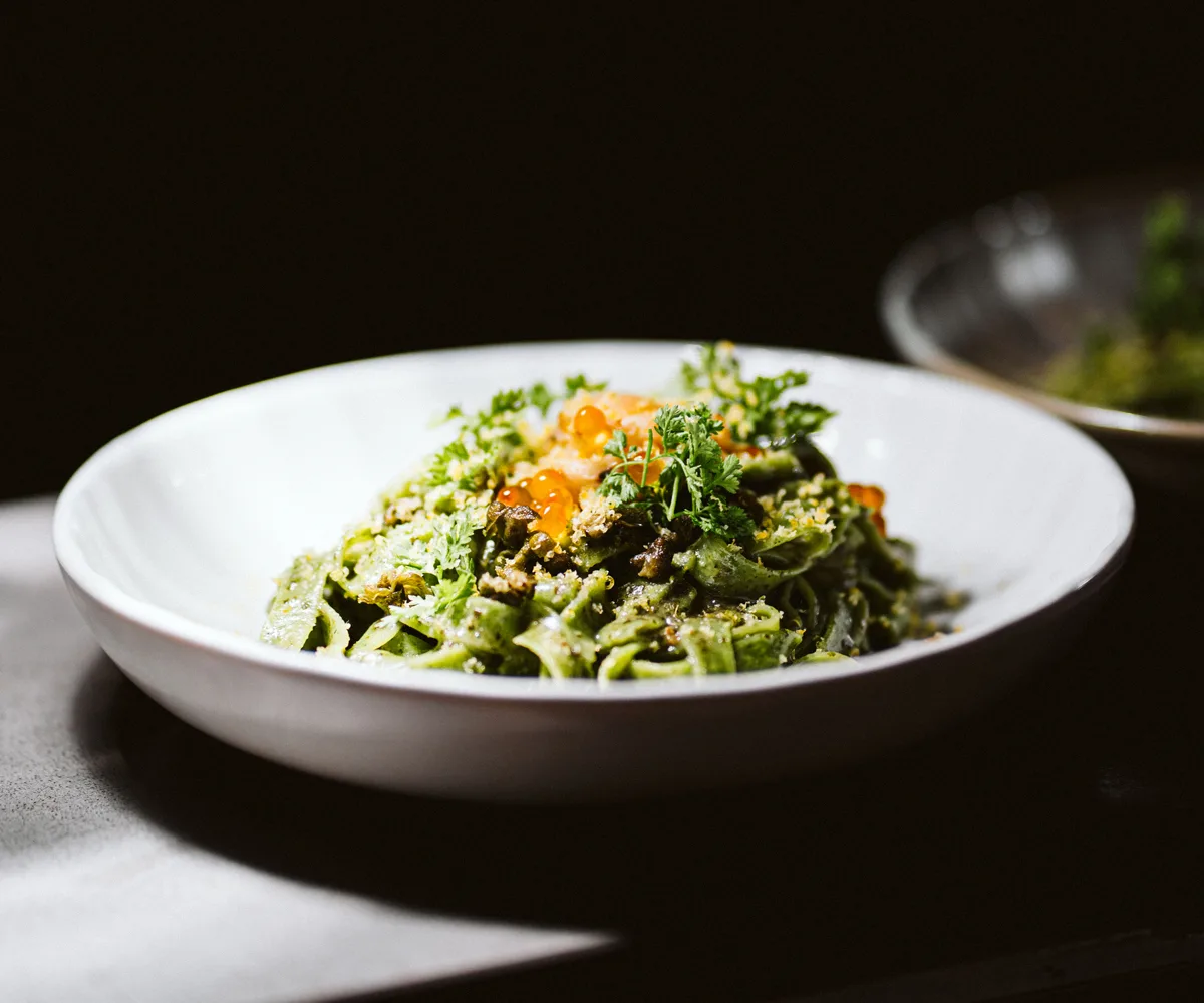 White bowl filled with pasta noodles in a green sauce topped with orange salmon roe