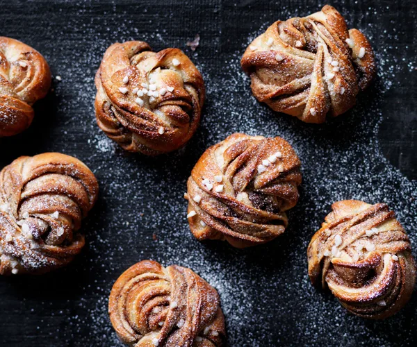 Six twisted buns, dusted with icing sugar, on a black background.